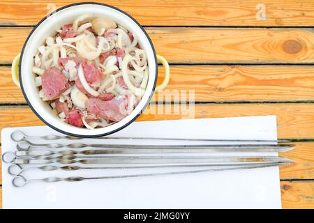 On the table is a pan in which are fresh red pieces of meat and chopped onions. Stock Photo