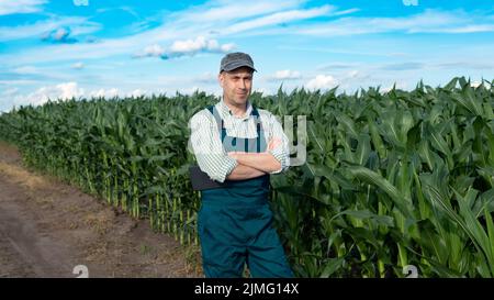 Middle age male caucasian confident satisfied farm worker in overalls with crossed arms stands at corn field Stock Photo