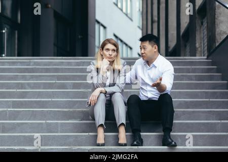 Business colleagues man and woman sitting together on stairs, Asian man comforting and comforting business woman, supporting Stock Photo