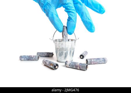 Gloved hand putting a used battery in a miniature steel bucket isolated on white background. Stock Photo