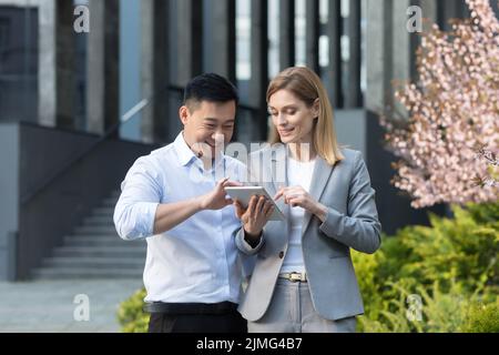 Two workers, Asian man and business woman, outside the office, smiling and happy, looking at the project implementation plan in the tablet computer Stock Photo