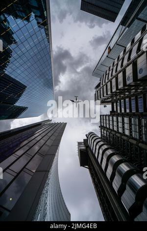 London, UK - 09 June 2022: Looking up to Lloyd's of London skyscraper while an airplane is flying over the buildings Stock Photo
