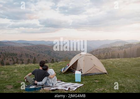 Rear on couple hugging and resting in mountains. On peak of mount, Beautiful view. Stock Photo