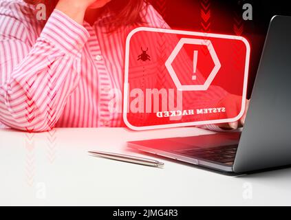 A woman sits at a laptop, in front of her is the inscription the system is hacked. User hacker attack, system hacking, password Stock Photo