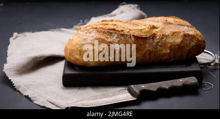Baked whole oval bread made from white wheat flour on a black table Stock Photo