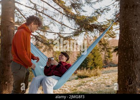 Young Caucasian man and woman laughing and having fun at hammock in wood. Happy together. Stock Photo