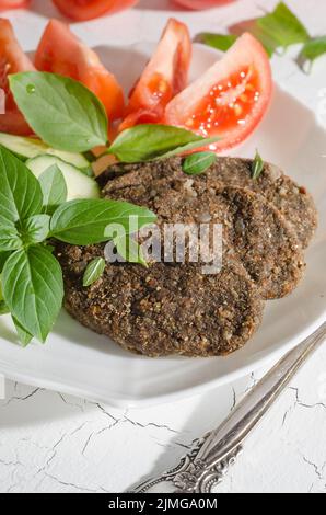 Raw cutlet made from vegetables and cereals with vegetables and herbs on a white plate with hard light Stock Photo