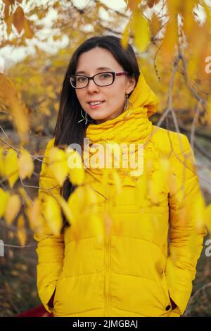 Beautiful woman in a yellow jacket and scarf on an autumn forest background Stock Photo