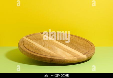 Round wooden kitchen pizza board on yellow-green background, utensils levitate Stock Photo