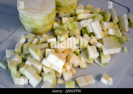 Healthy food, vegetables, peeled zucchini cut into rings and cubes are located on a white kitchen plastic board. Stock Photo