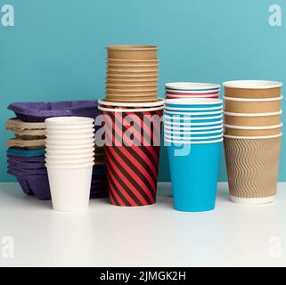 Stack of paper disposable multi-colored cups and stand on white table, blue background Stock Photo