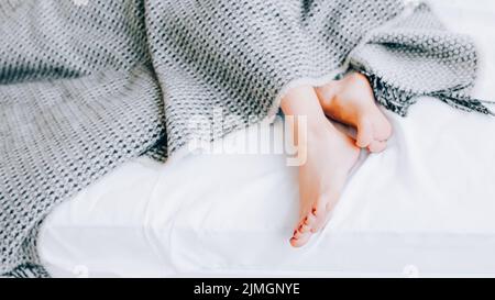 Foot care concept. Treatment and wellness. Beauty and relaxation. Female legs peeking out from blanket. Copy space. Stock Photo