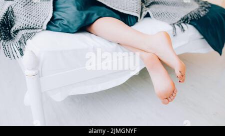 Foot hygiene concept. Treatment and wellness. Beauty and relaxation. Closeup of female legs peeking out from blanket. Stock Photo