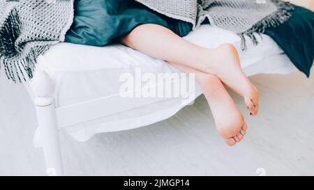 Foot hygiene concept. Treatment and wellness. Beauty and relaxation. Closeup of female legs peeking out from blanket. Stock Photo