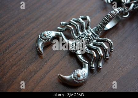 A small metal scorpion with carved ornaments is placed on a brown wooden table. Stock Photo