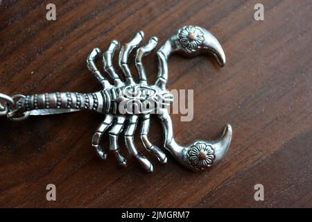 A small metal scorpion with carved ornaments is placed on a brown wooden table. Stock Photo