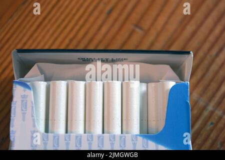 A pack of white thin cigarettes lying on a yellow wooden table Stock Photo 