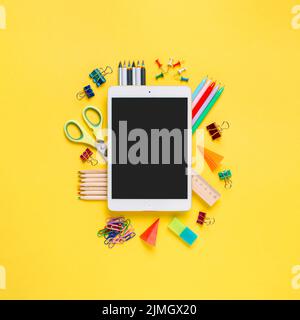 Online study, distantly learning class. Online education, back to school, freelancer work concept. Tablet pc and school supplies, stationery accessories on colored yellow background. Flatlay, top view Stock Photo