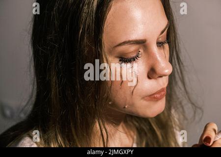 Crying young woman with cigarette in her hand against wall. Portrait of an unhappy woman experiencing an emotional crisis in life. Psychological Stock Photo