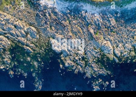 Aerial drone top view of ocean's beautiful waves crashing on the rocky island coast Stock Photo