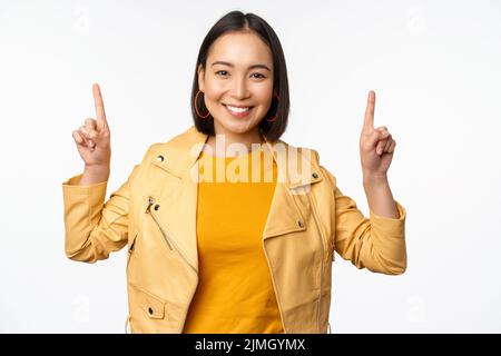 Enthusiastic asian girl pointing fingers up, showing advertisement on top, smiling happy, demonstrating promo offer or banner, s Stock Photo