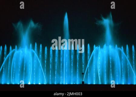 Beautiful fountain show. Large multi colored decorative dancing water jet led light fountain show at night. Dark background. Stock Photo