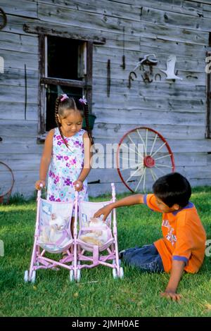 Two Native American children, sister and brother, play with twin kittens in a doll stroller on the Shoshone Bannock Indian Reservation, Fort Hall Idah