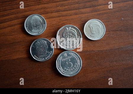 Ukrainian kopecks, small change in the amount of one 1, two 2, five 5 hryvnias are located on a dark brown table. Stock Photo