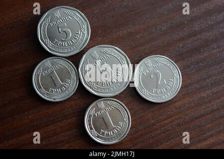 Ukrainian kopecks, small change in the amount of one 1, two 2, five 5 hryvnias are located on a dark brown table. Stock Photo