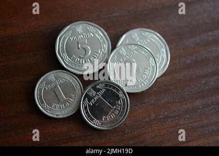 Ukrainian kopecks, small change in the amount of one 1, two 2, five 5 hryvnias are located on a dark brown table. Stock Photo