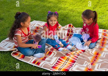 Three Native American girls, elementary age, play together on a blanket with Barbie dolls. Stock Photo