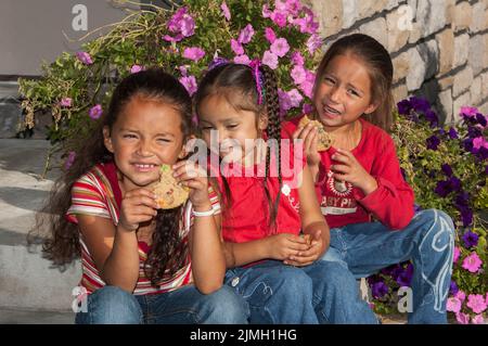 Three elementary age girls eat cookies for an after school snack.