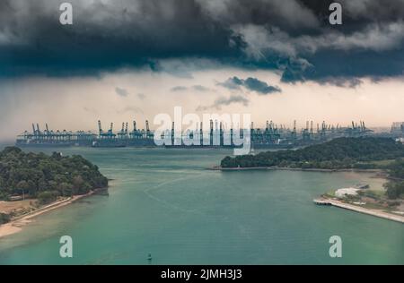 The huge busiest logistic port in Singapore, plenty of cranes to move containers, huge cargo ships in the background, skyscraper Stock Photo