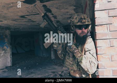 A bearded soldier in special forces uniform in dangerous military mission, refile his weapon while hiding from the wall. Selecti Stock Photo