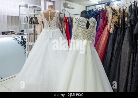 Two white wedding dresses on a background of dark evening dresses in a wedding dress shop. Stock Photo
