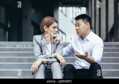 Two business colleagues Asian man and woman sitting on stairs talking and discussing in work break Stock Photo
