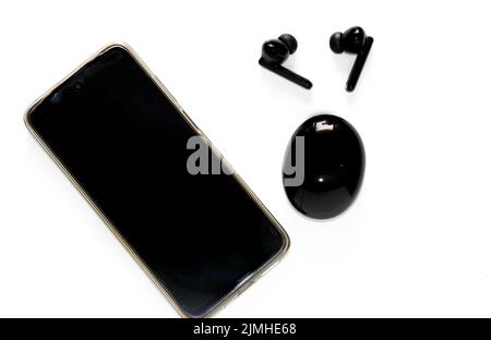 Top View Of Pair Of Black Wireless Earbuds And Smartphone In White Background Stock Photo