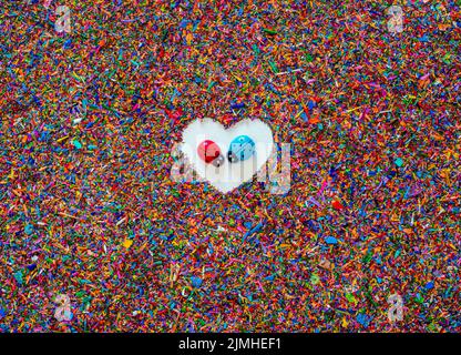 Textured background of colored crayon shavings with a white heart in the center and, in the middle of it, two ladybugs face to face with love Stock Photo