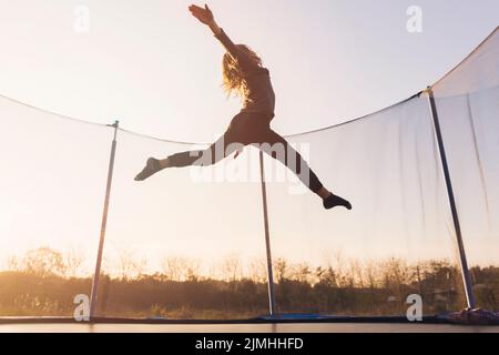 Active little girl jumping trampoline against sky Stock Photo