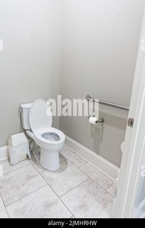 A small half bathroom with gray walls and a toilet with tile floors in a new construction house with a handicap railing Stock Photo