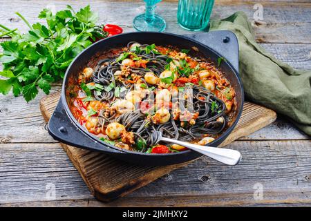 Traditional Italian spaghetti al nero di seppia with baby squid ink in tomato sauce served as close-up in a cast iron pan on a w Stock Photo