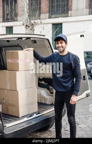 Portrait happy delivery man standing near vehicle with cardboard boxes Stock Photo