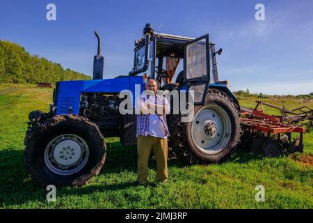 Farmer stands near the tractor on agricultural field Stock Photo