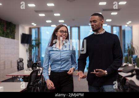 Two happy diverse professional executive business team people woman and African American man walking in coworking office. Multic Stock Photo