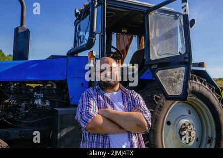 Satisfied farmer stands near the tractor on agricultural field after working Stock Photo