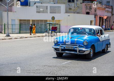 A light blue Chevrolet with white hard top, from the 1950's, traveling down a street. Havana, Cuba. Stock Photo