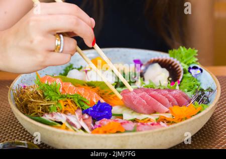 Woman eating delicious sashimi, closeup on chopsticks. Stock Photo