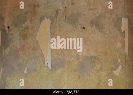 The texture of an aged concrete wall with a piece of wallpaper torn off. Grey-orange walls. Interior decoration at home, home renovation. Abstract background with construction concept. Stock Photo