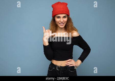 Photo of young positive happy smiling beautiful brunette curly woman with sincere emotions wearing black crop top and red hat is Stock Photo