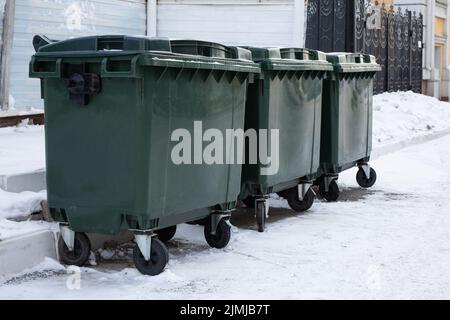 Green garbage containers in a row on the street covered with snow Stock Photo
